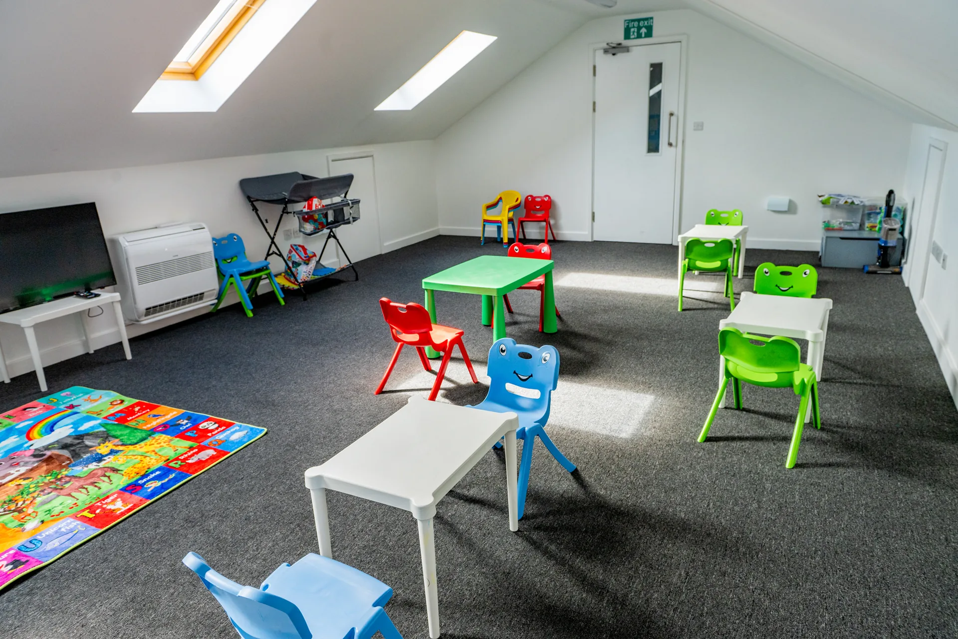 A bright children's room with colourful tables, chairs and a play mat
